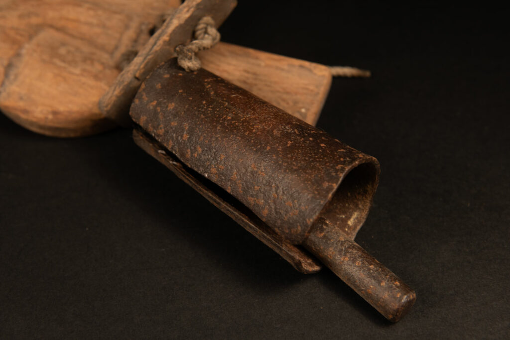 Rukai tribe alarm bell showing a wooden handle shaped with a human face linked with a cylindrical bell .