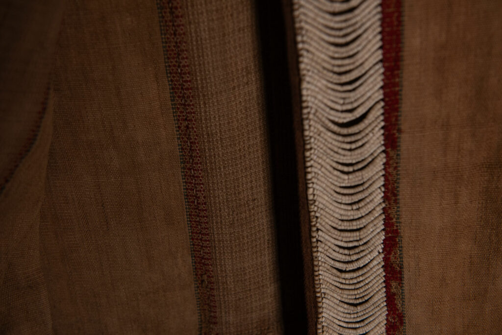 Long Atayal tribe sleeveless tunic with an open front and no collar. Made from linen and decorated with dark red wool, its most striking feature lies in the elaborate use of cylindrical clam-shell beads, which are carefully embedded into the fabric in both horizontal and vertical alignments.