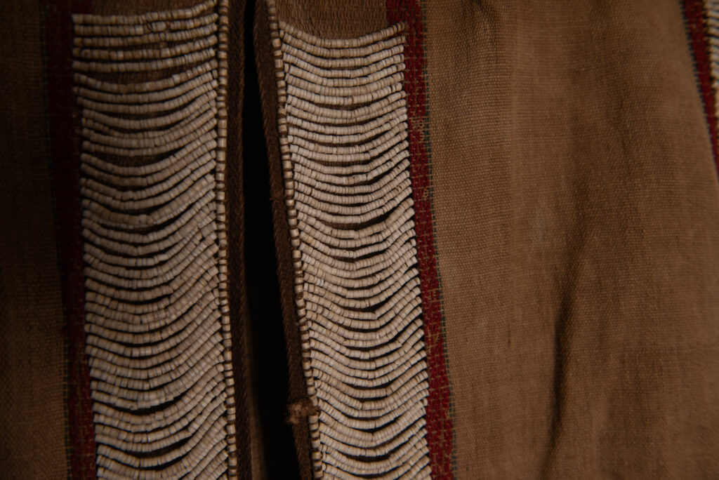 Long Atayal tribe sleeveless tunic with an open front and no collar. Made from linen and decorated with dark red wool, its most striking feature lies in the elaborate use of cylindrical clam-shell beads, which are carefully embedded into the fabric in both horizontal and vertical alignments.