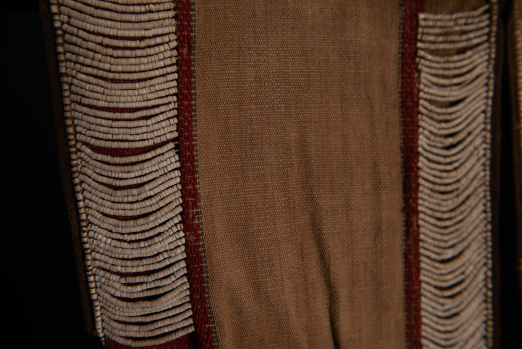 Long Atayal tribe sleeveless tunic with an open front and no collar. Made from linen and decorated with dark red wool, its most striking feature lies in the elaborate use of cylindrical clam-shell beads, which are carefully embedded into the fabric in both horizontal and vertical alignments.