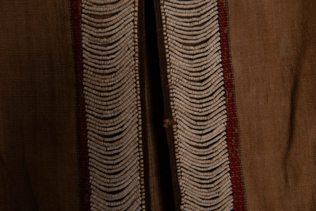Long Atayal tribe sleeveless tunic with an open front and no collar. Made from linen and decorated with dark red wool, its most striking feature lies in the elaborate use of cylindrical clam-shell beads, which are carefully embedded into the fabric in both horizontal and vertical alignments.