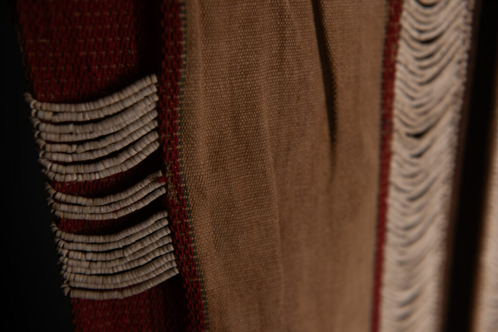 Long Atayal tribe sleeveless tunic with an open front and no collar. Made from linen and decorated with dark red wool, its most striking feature lies in the elaborate use of cylindrical clam-shell beads, which are carefully embedded into the fabric in both horizontal and vertical alignments.