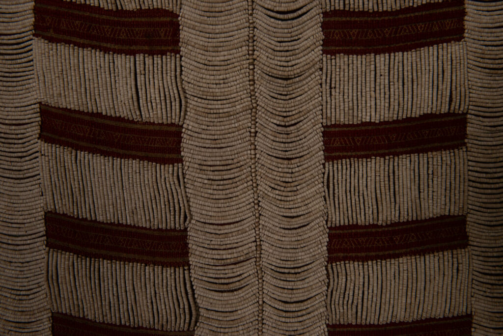 Long Atayal tribe sleeveless tunic with an open front and no collar. Made from linen and decorated with dark red wool, its most striking feature lies in the elaborate use of cylindrical clam-shell beads, which are carefully embedded into the fabric in both horizontal and vertical alignments.