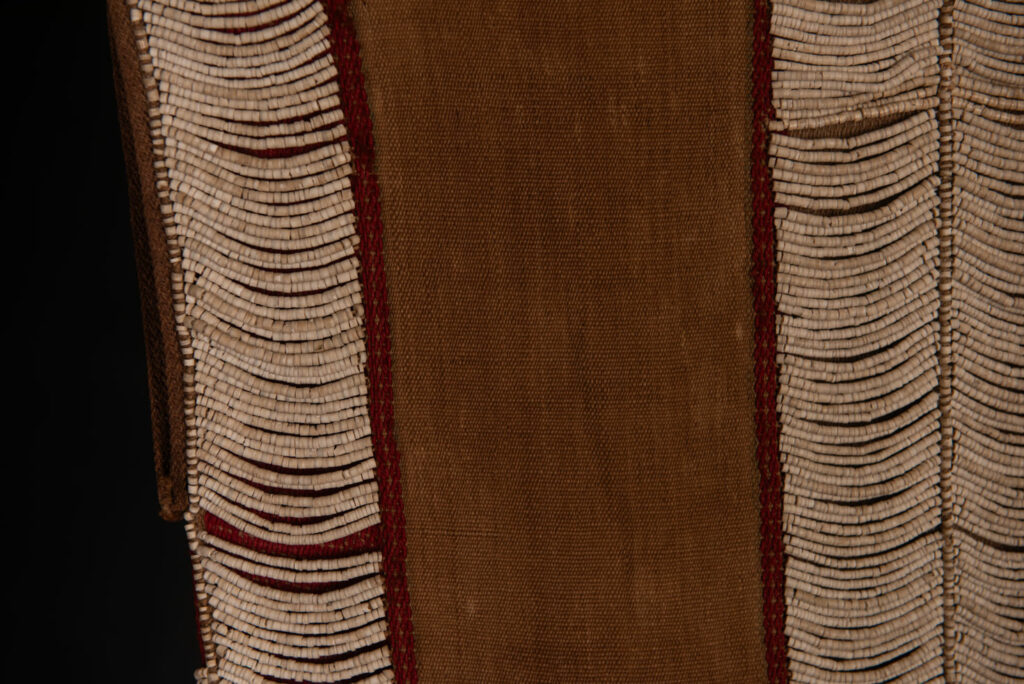 Long Atayal tribe sleeveless tunic with an open front and no collar. Made from linen and decorated with dark red wool, its most striking feature lies in the elaborate use of cylindrical clam-shell beads, which are carefully embedded into the fabric in both horizontal and vertical alignments.