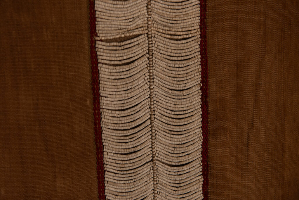 Long Atayal tribe sleeveless tunic with an open front and no collar. Made from linen and decorated with dark red wool, its most striking feature lies in the elaborate use of cylindrical clam-shell beads, which are carefully embedded into the fabric in both horizontal and vertical alignments.