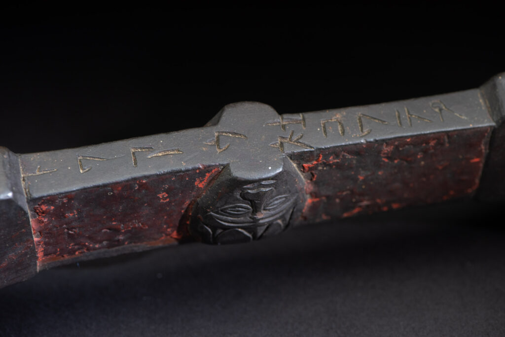 This linked cup from the Paiwan tribe features a diamond-shaped mouth and a central handle adorned with a carved human head. It is decorated with traditional black and red pigments.