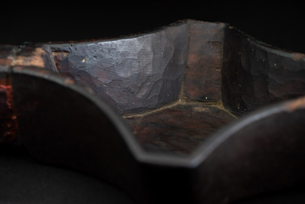 This linked cup from the Paiwan tribe features a diamond-shaped mouth and a central handle adorned with a carved human head. It is decorated with traditional black and red pigments.