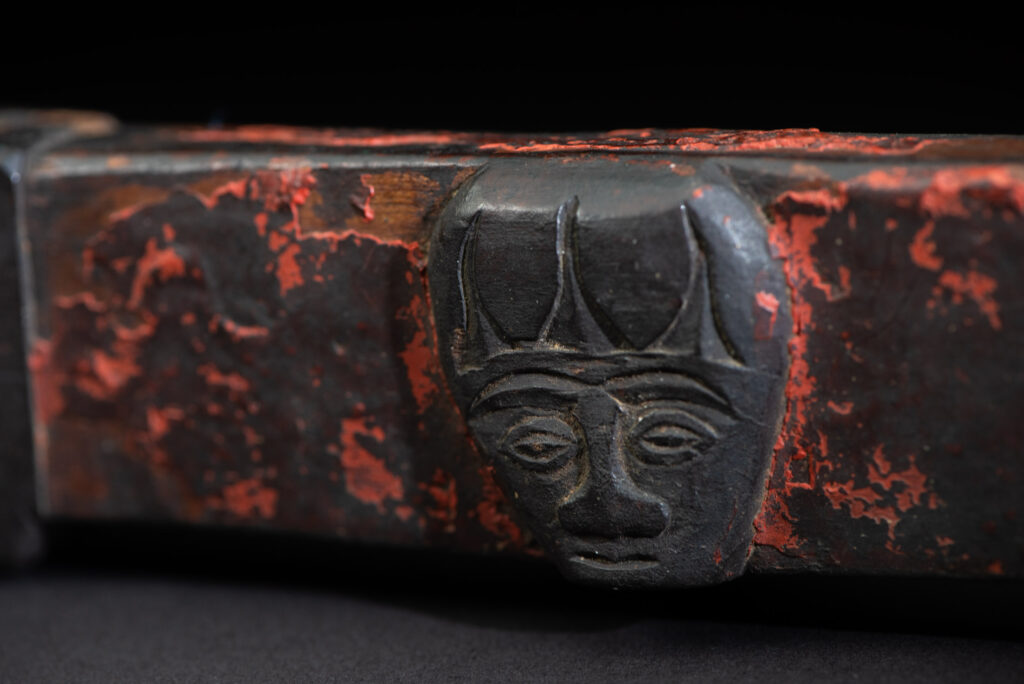 This linked cup from the Paiwan tribe features a diamond-shaped mouth and a central handle adorned with a carved human head. It is decorated with traditional black and red pigments.