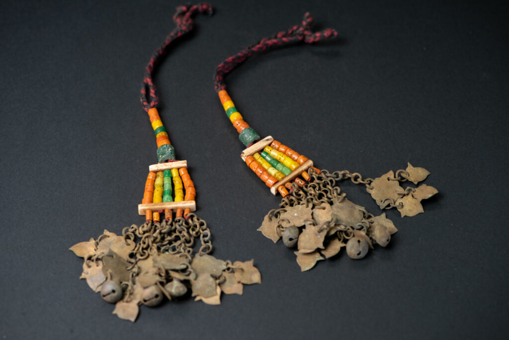 Pair of earrings from the Paiwan tribe, made of orange, yellow, and green beads, ending in six brass chains holding small bells and brass leaves.