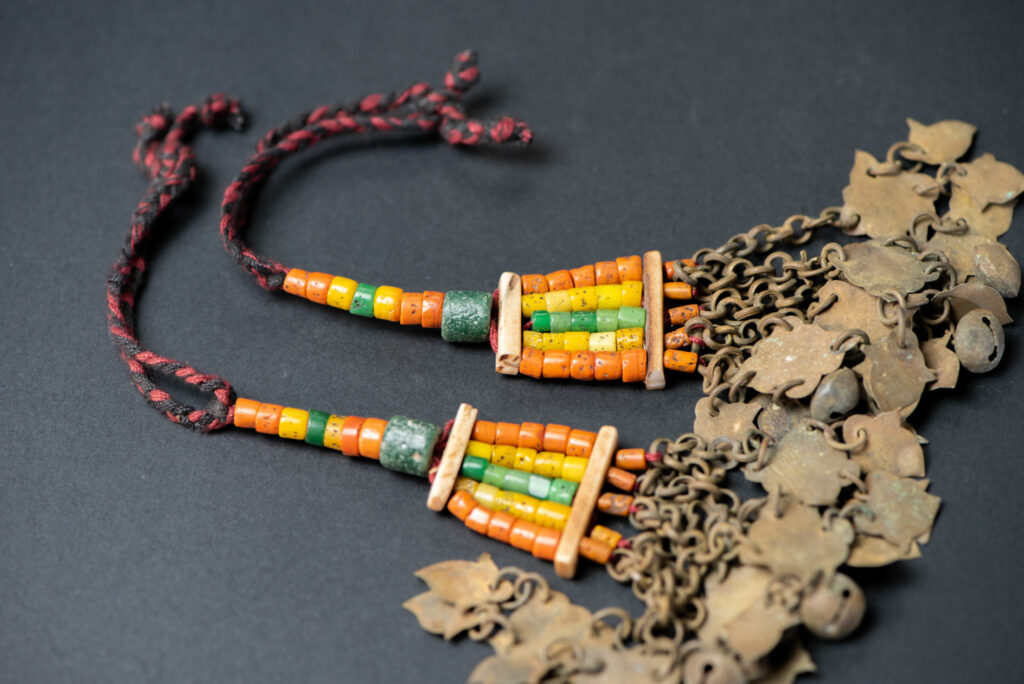 Pair of earrings from the Paiwan tribe, made of orange, yellow, and green beads, ending in six brass chains holding small bells and brass leaves.