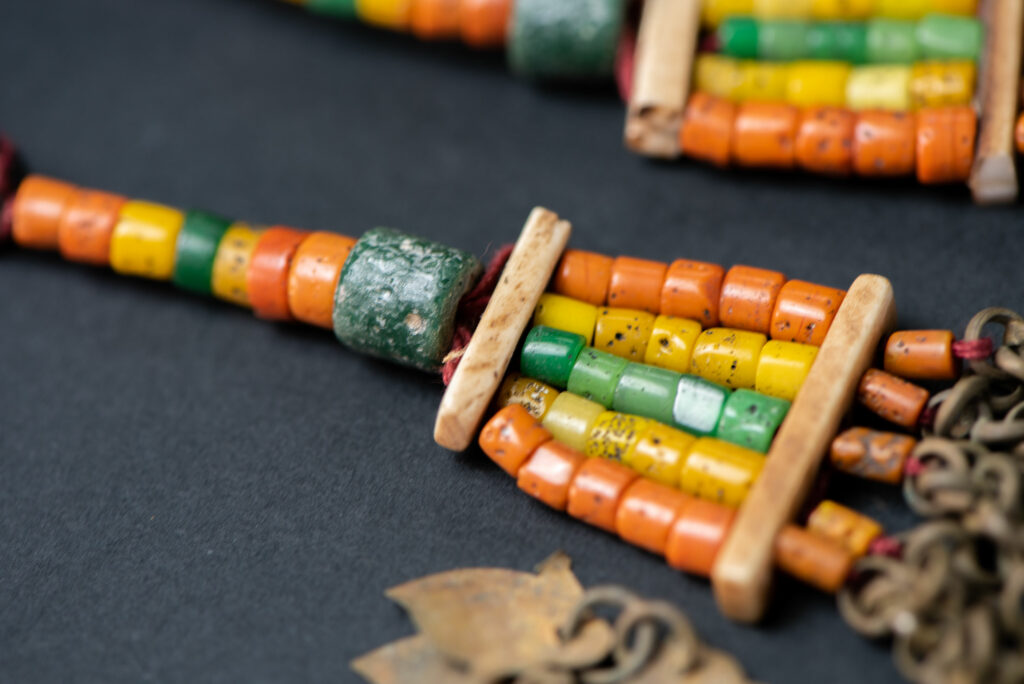 Pair of earrings from the Paiwan tribe, made of orange, yellow, and green beads, ending in six brass chains holding small bells and brass leaves.