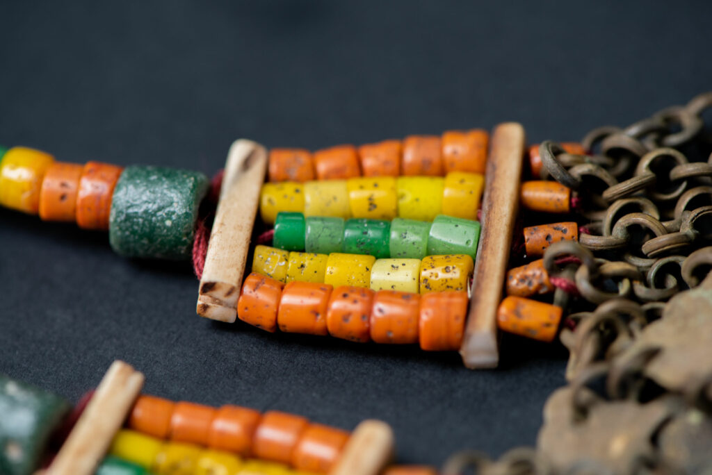 Pair of earrings from the Paiwan tribe, made of orange, yellow, and green beads, ending in six brass chains holding small bells and brass leaves.