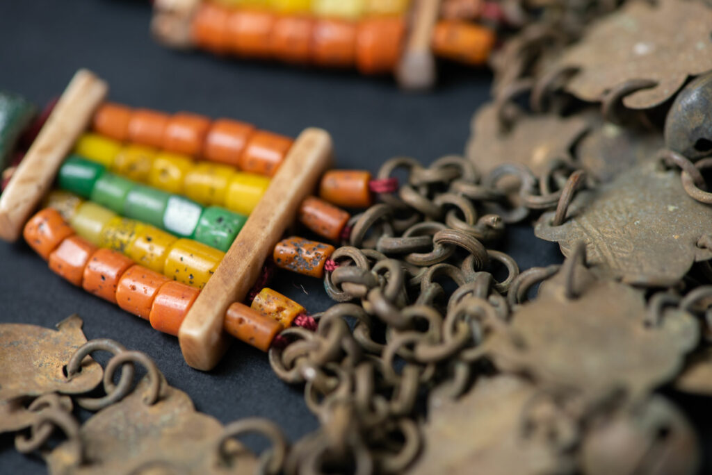 Pair of earrings from the Paiwan tribe, made of orange, yellow, and green beads, ending in six brass chains holding small bells and brass leaves.