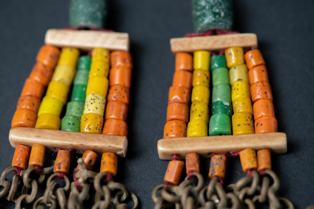 Pair of earrings from the Paiwan tribe, made of orange, yellow, and green beads, ending in six brass chains holding small bells and brass leaves.