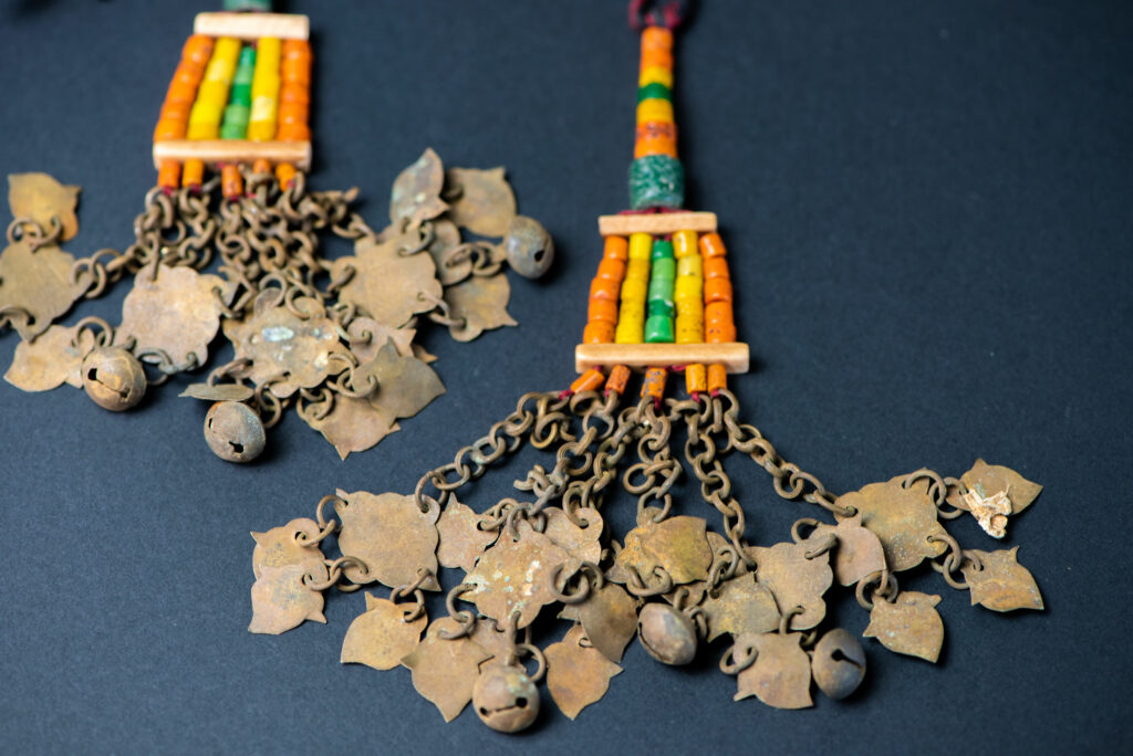 Pair of earrings from the Paiwan tribe, made of orange, yellow, and green beads, ending in six brass chains holding small bells and brass leaves.