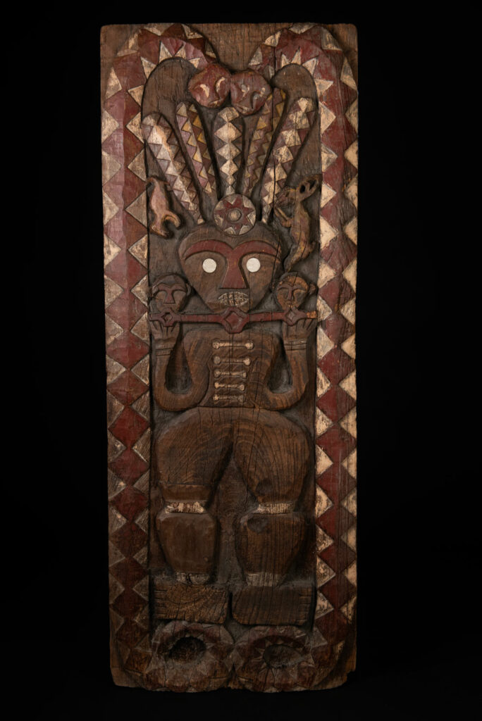 Panel from the Paiwan tribe depicting an ancestor in ceremonial attire, wearing a headdress adorned with eagle feathers. The panel is painted in red and white.
