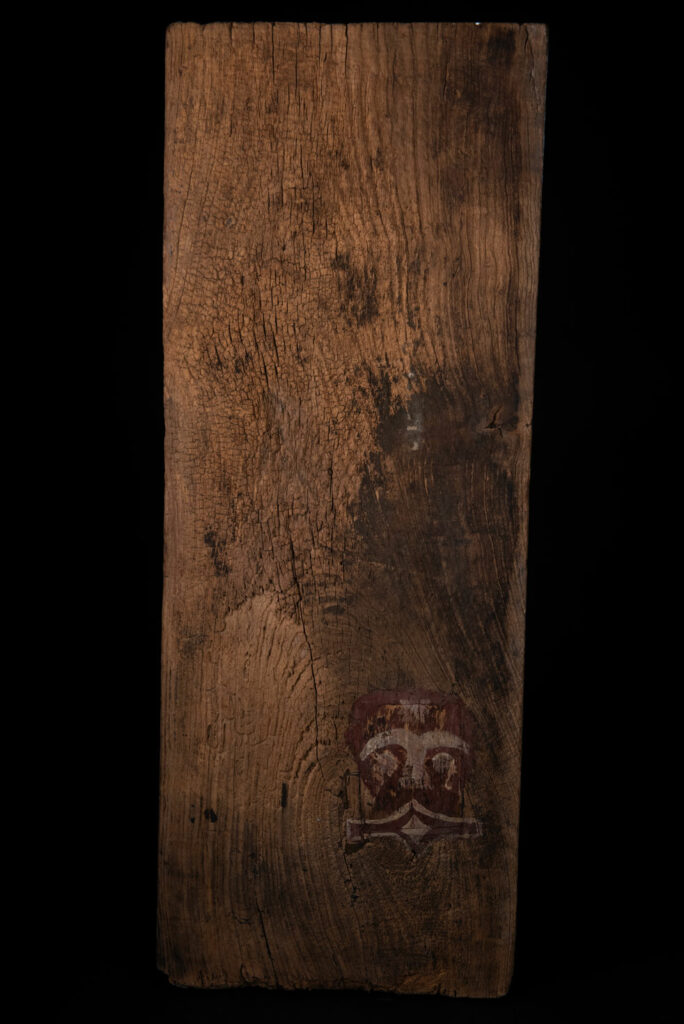 Panel from the Paiwan tribe depicting an ancestor in ceremonial attire, wearing a headdress adorned with eagle feathers. The panel is painted in red and white.