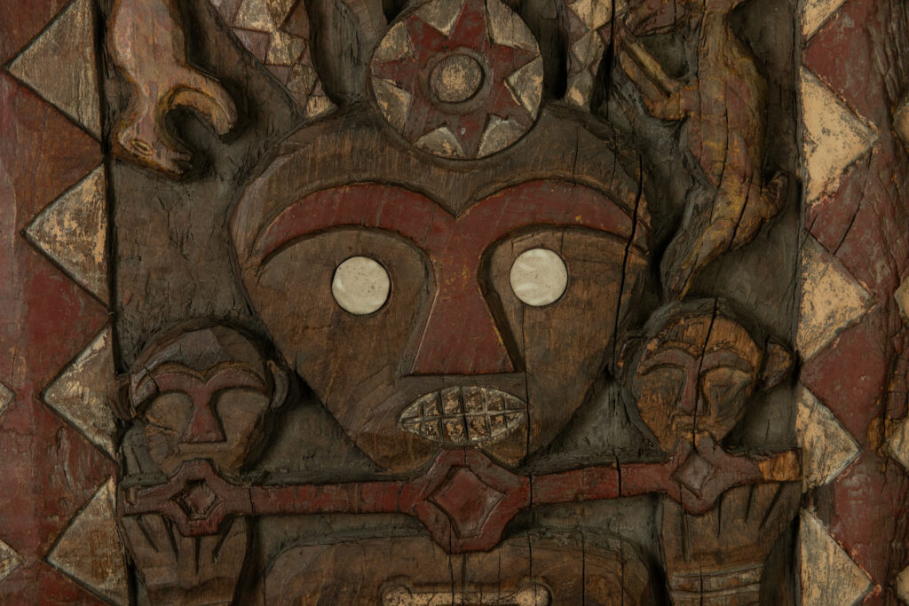 Panel from the Paiwan tribe depicting an ancestor in ceremonial attire, wearing a headdress adorned with eagle feathers. The panel is painted in red and white.