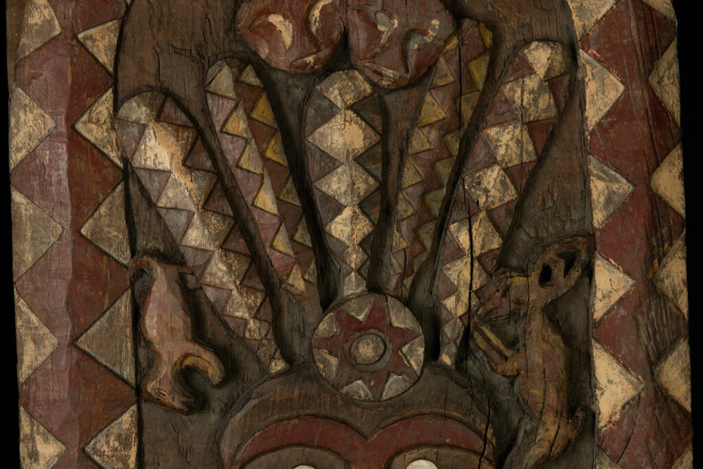 Panel from the Paiwan tribe depicting an ancestor in ceremonial attire, wearing a headdress adorned with eagle feathers. The panel is painted in red and white.