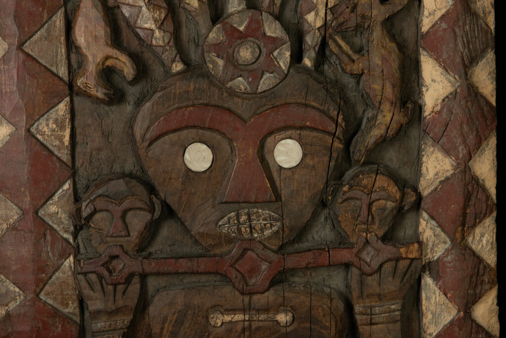 Panel from the Paiwan tribe depicting an ancestor in ceremonial attire, wearing a headdress adorned with eagle feathers. The panel is painted in red and white.