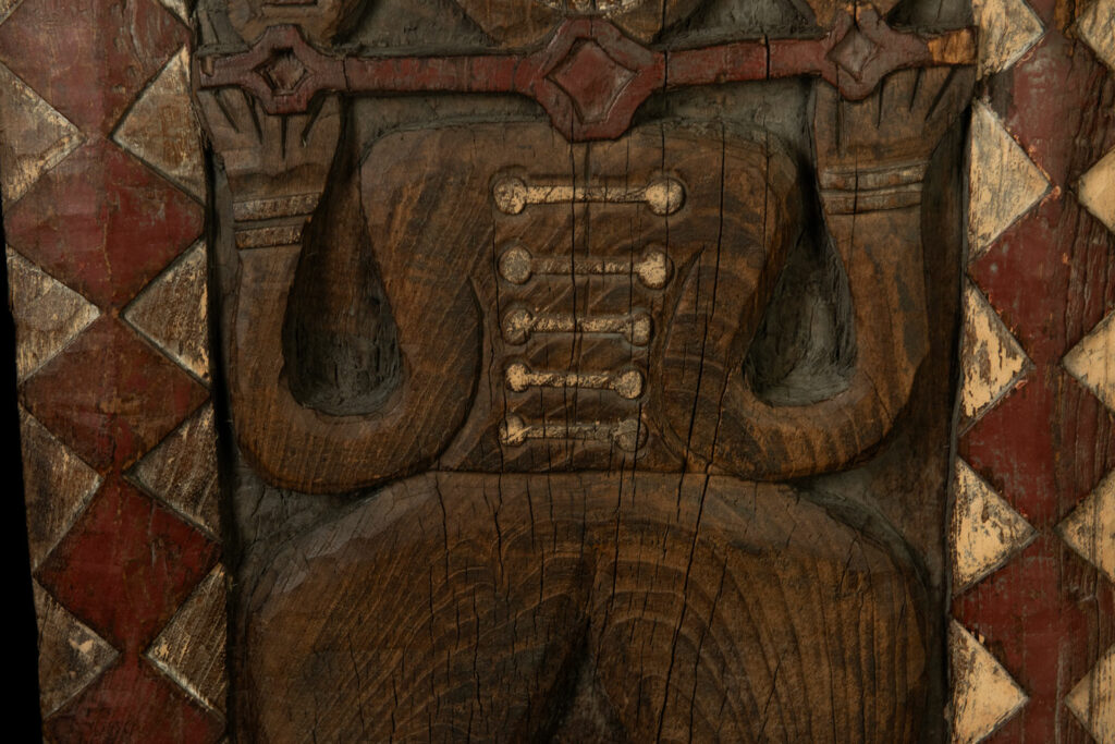 Panel from the Paiwan tribe depicting an ancestor in ceremonial attire, wearing a headdress adorned with eagle feathers. The panel is painted in red and white.