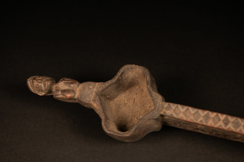 This drinking cup from paiwan features two beautifully carved handles, each depicting an ancestor holding the drinking cup between his thighs. The center of the double cup is carved with four human faces and a decorative frieze. The entire piece is made of natural wood.