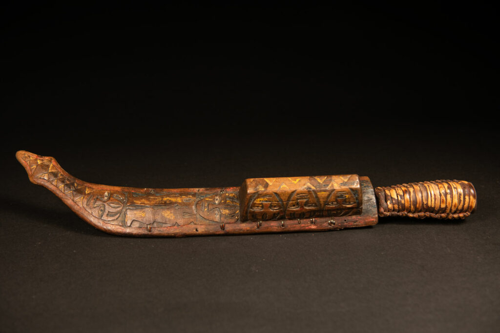 Sword from the Paiwan tribe, carved with stylized standing human figures, a serpent, and three faces. The blade and handle are forged from a single piece of iron.