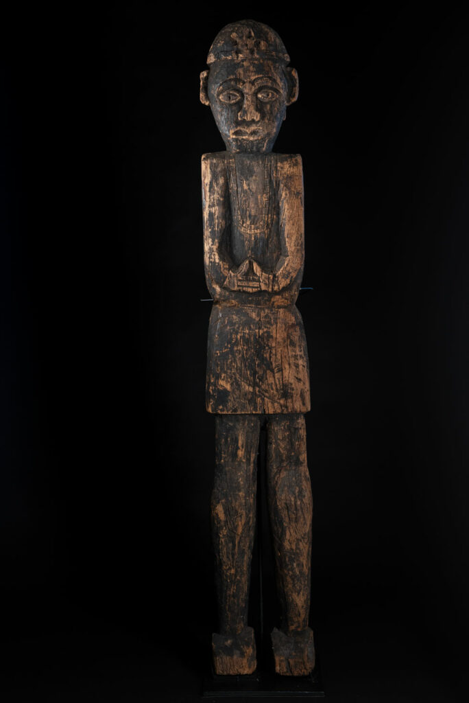 Tall ancient Paiwan tribe statue of an ancestor wearing a Paiwan dress , a hat - decoration of the hat are missing- and a bead collar.