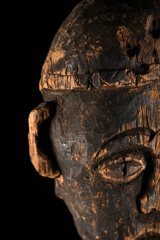 Tall ancient Paiwan tribe statue of an ancestor wearing a Paiwan dress , a hat - decoration of the hat are missing- and a bead collar.