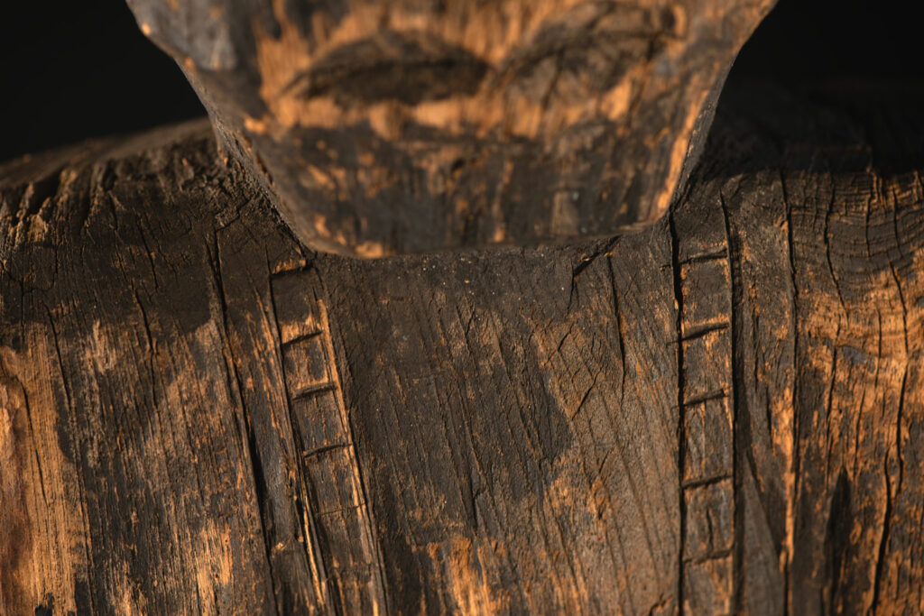 Tall ancient Paiwan tribe statue of an ancestor wearing a Paiwan dress , a hat - decoration of the hat are missing- and a bead collar.