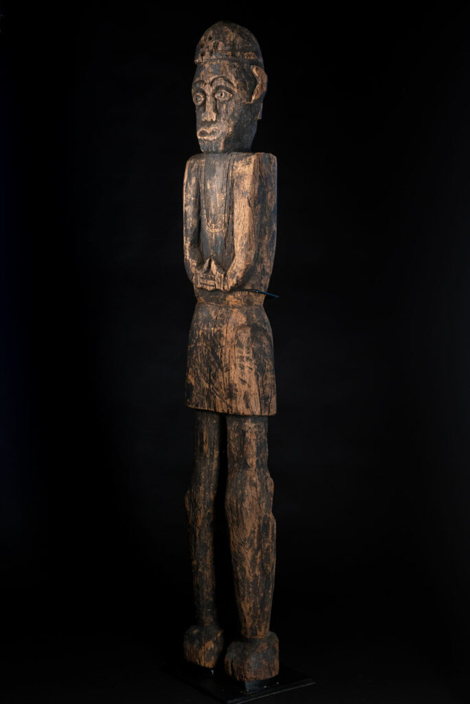 Tall ancient Paiwan tribe statue of an ancestor wearing a Paiwan dress , a hat - decoration of the hat are missing- and a bead collar.