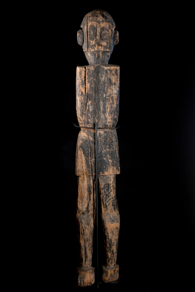 Massive Paiwan statue depicting a male ancestor wearing a short waistcloth , a jacket adorned with a sacred bead collar and a leather Hat.