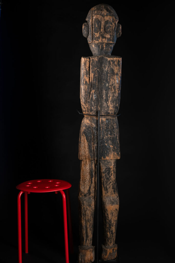 Tall ancient Paiwan tribe statue of an ancestor wearing a Paiwan dress , a hat - decoration of the hat are missing- and a bead collar.