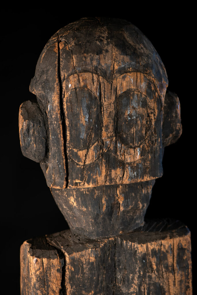 Tall ancient Paiwan tribe statue of an ancestor wearing a Paiwan dress , a hat - decoration of the hat are missing- and a bead collar.