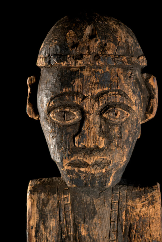 Tall ancient Paiwan tribe statue of an ancestor wearing a Paiwan dress , a hat - decoration of the hat are missing- and a bead collar.