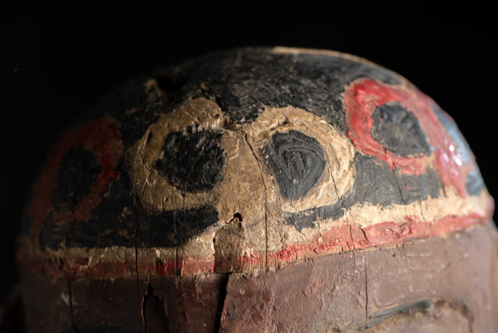 Wooden Statue from the Paiwan tribe painted in red, beige, and black, depicting a full-standing ancestor wearing ceremonial clothing and a leather headdress, with a knife at the waist.