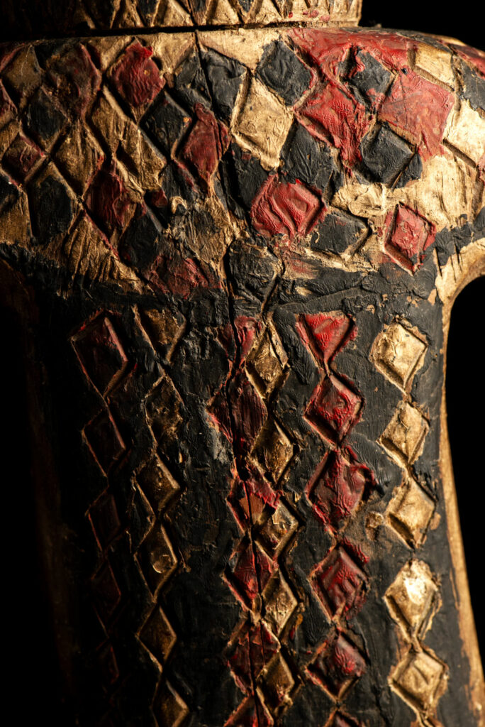 Wooden Statue from the Paiwan tribe painted in red, beige, and black, depicting a full-standing ancestor wearing ceremonial clothing and a leather headdress, with a knife at the waist.