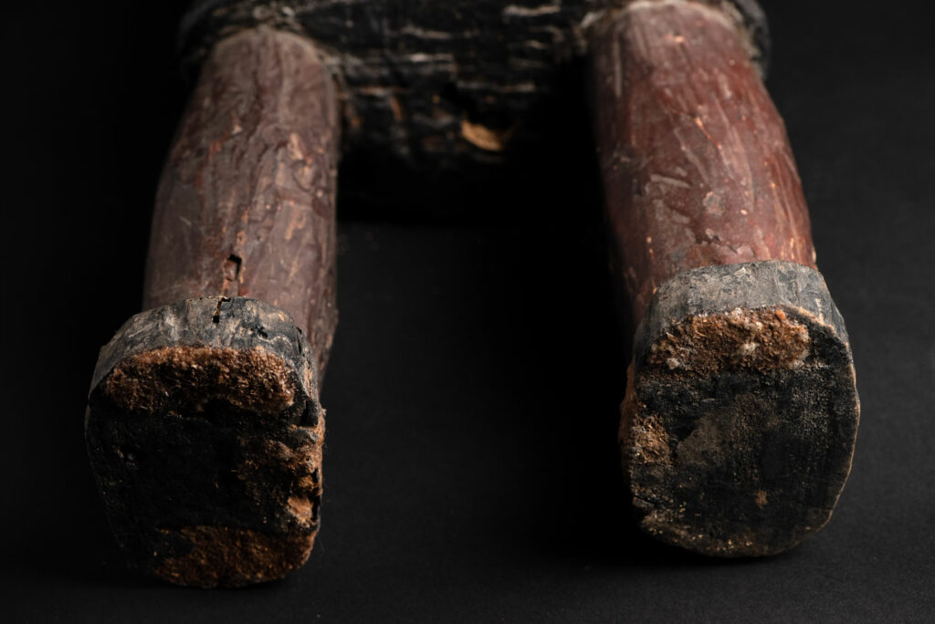 Wooden Statue from the Paiwan tribe painted in red, beige, and black, depicting a full-standing ancestor wearing ceremonial clothing and a leather headdress, with a knife at the waist.