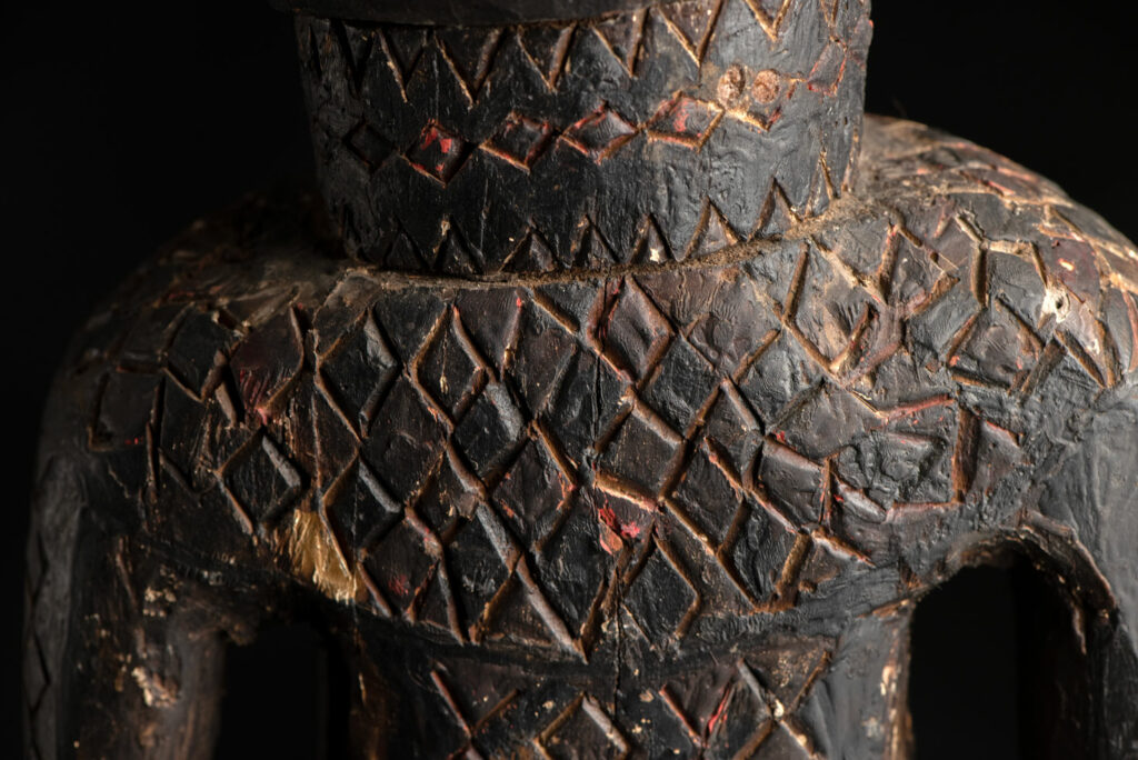 Wooden Statue from the Paiwan tribe painted in red, beige, and black, depicting a full-standing ancestor wearing ceremonial clothing and a leather headdress, with a knife at the waist.