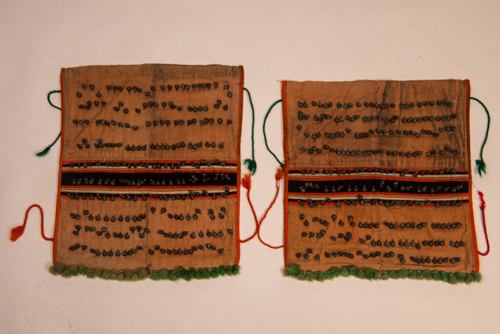 Pair of women’s legging from the Ami tribe, made of pink cotton fabric with orange and black stripes, sewn with ten rows of small bells. The bottom of each piece is adorned with green woolen knots. Such ankle ornaments were worn by women during ceremonies and festivals. This pair is estimated to date from the 1950s.