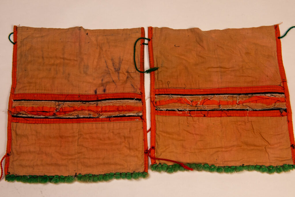 Pair of women’s legging from the Ami tribe, made of pink cotton fabric with orange and black stripes, sewn with ten rows of small bells. The bottom of each piece is adorned with green woolen knots. Such ankle ornaments were worn by women during ceremonies and festivals. This pair is estimated to date from the 1950s.