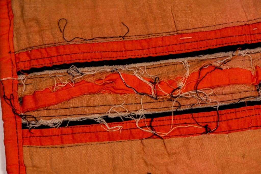 Pair of women’s legging from the Ami tribe, made of pink cotton fabric with orange and black stripes, sewn with ten rows of small bells. The bottom of each piece is adorned with green woolen knots. Such ankle ornaments were worn by women during ceremonies and festivals. This pair is estimated to date from the 1950s.