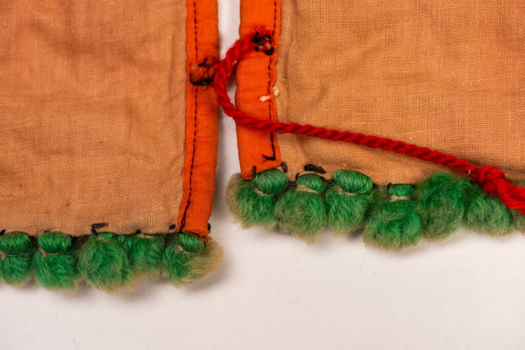Pair of women’s legging from the Ami tribe, made of pink cotton fabric with orange and black stripes, sewn with ten rows of small bells. The bottom of each piece is adorned with green woolen knots. Such ankle ornaments were worn by women during ceremonies and festivals. This pair is estimated to date from the 1950s.