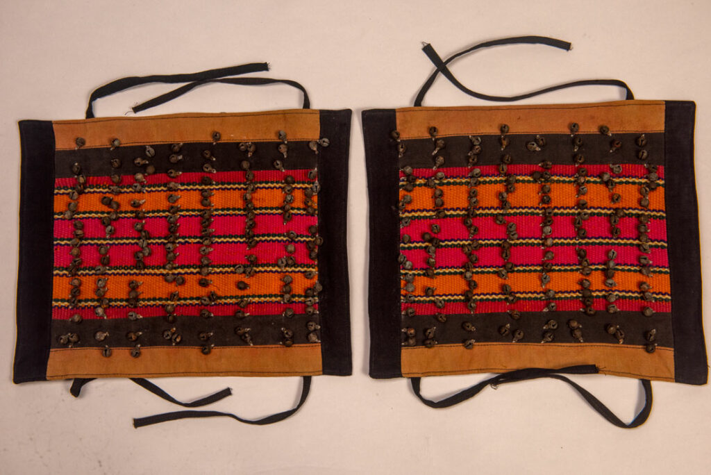 Antique Paiwan tribe women’s leggings made of red wool with black cotton panels and vertical stripes in pink, yellow, and orange. This traditional pair features eight rows of small copper bells and black cotton straps for tying around the calves. Such square leggings were worn over skirts to expose the lower legs and were decorated only by noblewomen. A rare example of formal Paiwan ceremonial wear from Taiwan's Indigenous heritage.