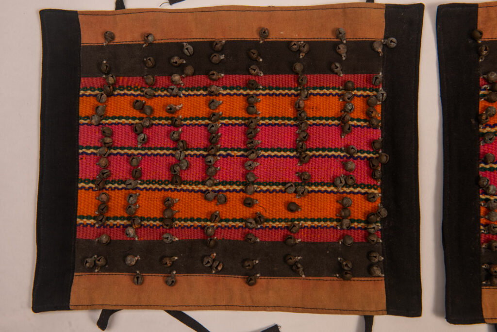 Antique Paiwan tribe women’s leggings made of red wool with black cotton panels and vertical stripes in pink, yellow, and orange. This traditional pair features eight rows of small copper bells and black cotton straps for tying around the calves. Such square leggings were worn over skirts to expose the lower legs and were decorated only by noblewomen. A rare example of formal Paiwan ceremonial wear from Taiwan's Indigenous heritage.