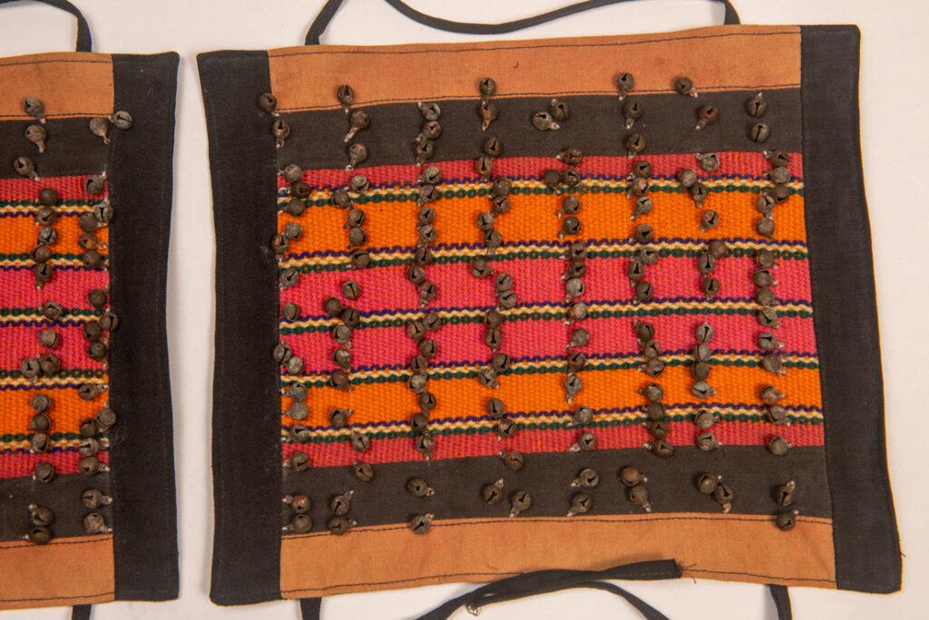 Antique Paiwan tribe women’s leggings made of red wool with black cotton panels and vertical stripes in pink, yellow, and orange. This traditional pair features eight rows of small copper bells and black cotton straps for tying around the calves. Such square leggings were worn over skirts to expose the lower legs and were decorated only by noblewomen. A rare example of formal Paiwan ceremonial wear from Taiwan's Indigenous heritage.