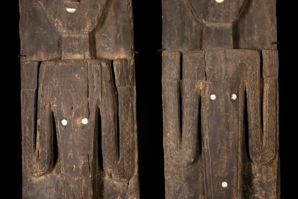 Pair of Paiwan Tribe Ancestor Panels, likely from Laiyi, carved with two figures—a male and a female. Their eyes, mouth, nipples, and navel are inlaid with porcelain. Their arms and legs are decorated with tribal motifs suggesting tattoos. Both figures wear hats, and the snakes carved above their heads indicate that they were important members of the nobility.