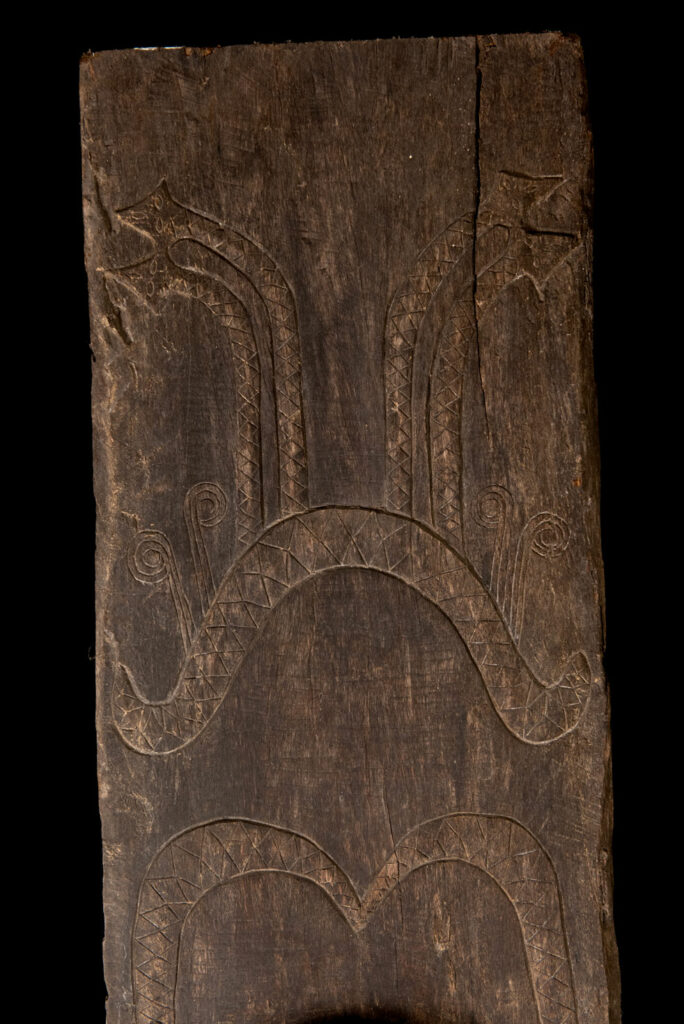 Pair of Paiwan Tribe Ancestor Panels, likely from Laiyi, carved with two figures—a male and a female. Their eyes, mouth, nipples, and navel are inlaid with porcelain. Their arms and legs are decorated with tribal motifs suggesting tattoos. Both figures wear hats, and the snakes carved above their heads indicate that they were important members of the nobility.