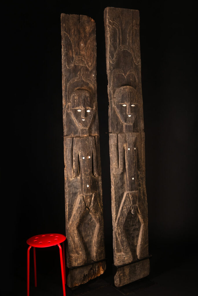 Pair of Paiwan Tribe Ancestor Panels, likely from Laiyi, carved with two figures—a male and a female. Their eyes, mouth, nipples, and navel are inlaid with porcelain. Their arms and legs are decorated with tribal motifs suggesting tattoos. Both figures wear hats, and the snakes carved above their heads indicate that they were important members of the nobility.