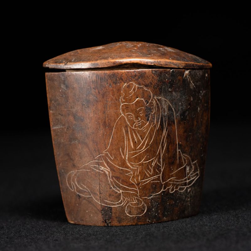 Wooden belt snuffbox from the Pingpu tribes, decorated with an engraving of a Chinese sage. It features a hinged lid carved from a single piece of wood and a section designed for attachment to the belt.